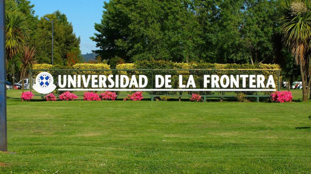 Letrero de la Universidad de La Frontera sobre un seto, con flores rosadas y árboles detrás, en el campus Andrés Bello de Temuco.